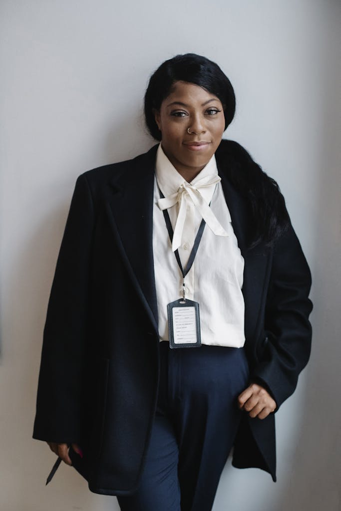 Positive black woman in formal suit standing against white wall